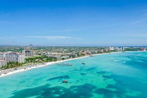 A coastal cityscape with a beach, clear turquoise waters, and several high-rise buildings.