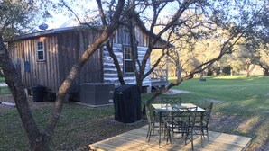 A rustic wooden cabin with a deck, outdoor seating, and a large air conditioning unit. - Secluded Log Cabin for Two in La Grange TX (La Grange)