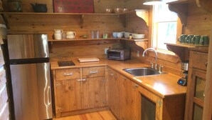 A compact kitchen with wooden cabinets, a stainless steel refrigerator, a toaster, and a sink. - Secluded Log Cabin for Two in La Grange TX (La Grange)