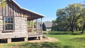A rustic log cabin with a porch, surrounded by a well-maintained lawn and trees. - Secluded Log Cabin for Two in La Grange TX (La Grange)