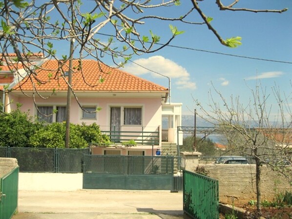 A two-story house with a red-tiled roof, a balcony, and a view of the sea.