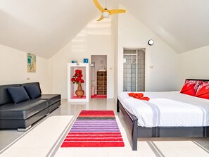 A modern bedroom with a bed, a sofa, a red and purple striped rug, a ceiling fan, and a white door leading to a bathroom. - Luxury Private pool Villa Nap Dau Perfect for Groups (Chalong,Tambon Wichit)