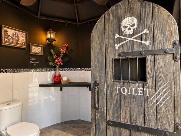 A rustic bathroom with a wooden door labeled 'TOILET' and a sign above it.