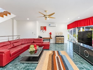 A modern living room with a red sectional sofa, a coffee table with flowers, a flat-screen TV, and a ceiling fan. - Luxury Private pool Villa Nap Dau Perfect for Groups (Chalong,Tambon Wichit)