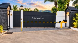 A gated entrance with a sign reading 'Villa Napo Dau' and a CCTV camera on the left.