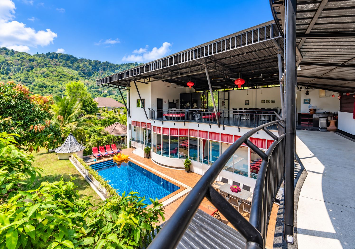 Un edificio de dos pisos con piscina, mobiliario exterior y vistas a un paisaje verde exuberante.