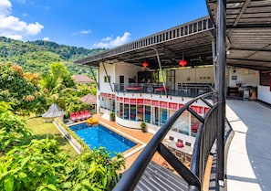 A two-story building with a swimming pool, outdoor seating, and a view of a lush green landscape. - Luxury Private pool Villa Nap Dau Perfect for Groups (Chalong,Tambon Wichit)