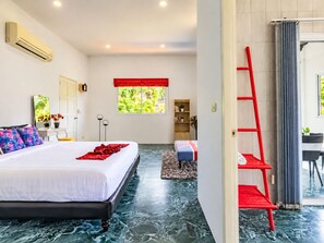 A modern bedroom with a large bed, a red ladder, a small seating area, and a view of greenery outside. - Luxury Private pool Villa Nap Dau Perfect for Groups (Chalong,Tambon Wichit)