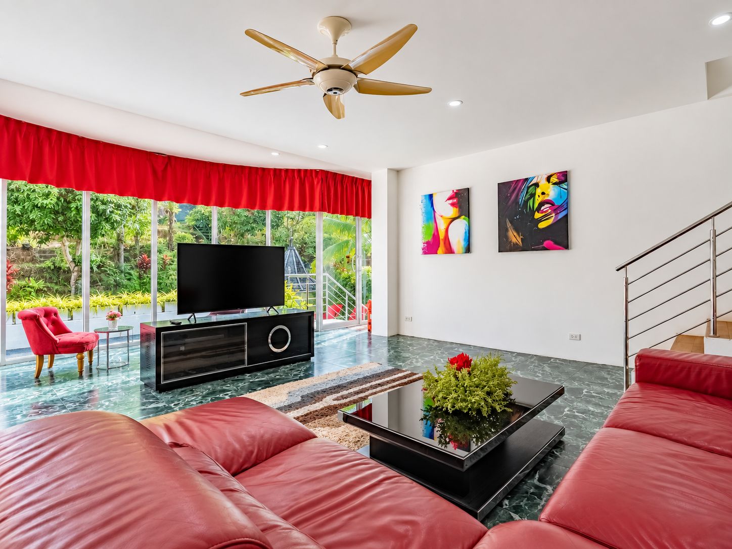 Una sala de estar moderna con un televisor de pantalla plana, sofás tapizados en rojo, un ventilador de techo y obras de arte en las paredes.