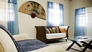 Una sala de estar con un sofá, una mesa de centro de vidrio y un ventilador en la pared.