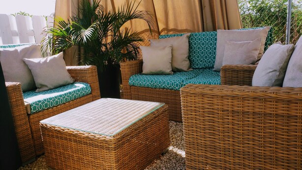 Un conjunto de sofá de mimbre con cojines estampados, una mesita y una planta en maceta.