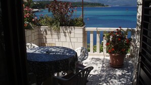 Un balcon avec une table et des chaises, donnant sur une mer bleue et limpide et sur des montagnes.