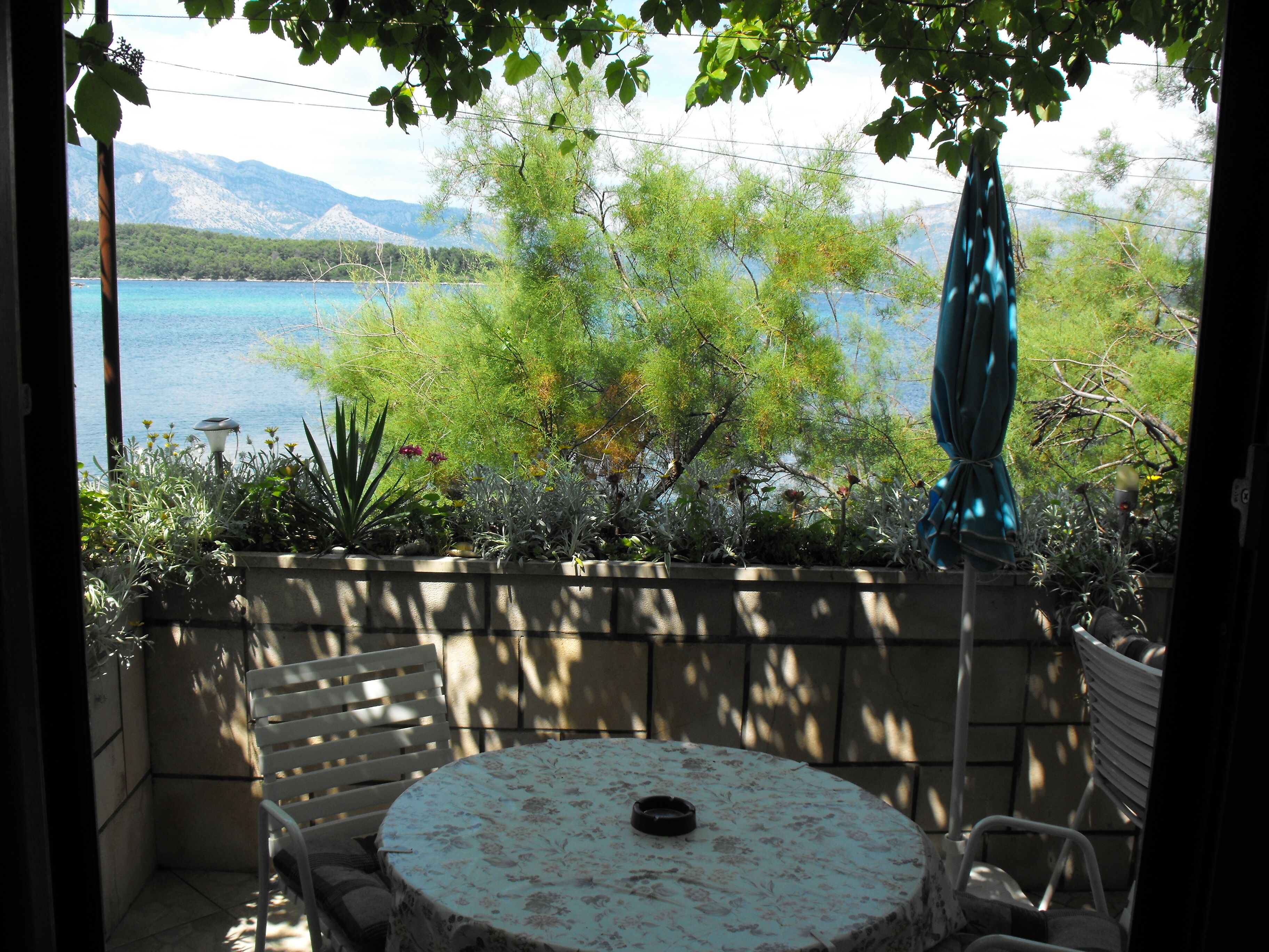 A patio with a round table and chairs, overlooking a body of water and mountains.