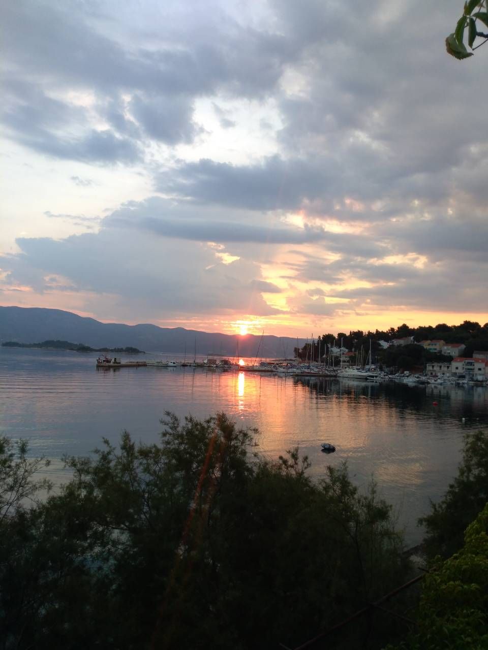 A marina with boats docked, a sunset in the background, and a calm body of water.