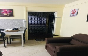 Ein Wohnzimmer mit braunem Sofa, einem Esstisch mit Stühlen und einer Küchenzeile mit Fliesenrückwand.