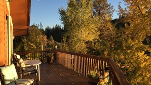 A wooden deck with outdoor seating, surrounded by trees and a clear sky. - Premier Chalet Home on Beautiful Williams Lake - Consistently #1 in Region.  (Cheney)
