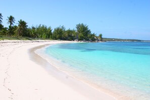Ein Strand mit klarem türkisblauem Wasser, weißem Sand und Palmen.
