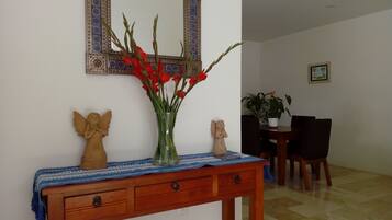 A wooden console table with a vase of red flowers, angelic sculptures, and a mirror with a decorative frame.