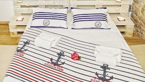 Un dormitorio con techo inclinado y tragaluces, vigas de madera, una cama con ropa de cama a rayas y vista a un cuerpo de agua.