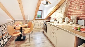 Una cocina acogedora con pared de piedra, vigas de madera, una mesa de comedor de madera con sillas y una encimera con cafetera y fruta.