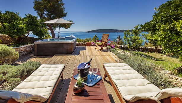 Een houten terras met twee lounge stoelen, een jacuzzi en een tafel met een dienblad en glas.