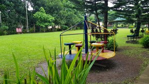 A playground with a rotating platform and benches, surrounded by a well-maintained lawn and trees. - Tagaytay Summer House (Tagaytay)