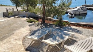 A patio with two lounge chairs, a small tree, and a boat docked by the water. - Traditional Istrian stone villa – 'Villa Ane' - Rakalj (Rakalj)