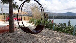 A swing chair suspended from a metal frame, a red car parked in the background, and a body of water with a red lighthouse in the distance. - Traditional Istrian stone villa – 'Villa Ane' - Rakalj (Rakalj)
