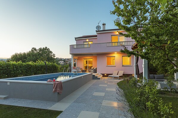 Une maison à deux étages avec une piscine, un espace salon extérieur et un jardin.