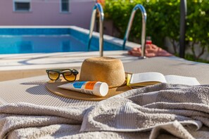 Escena junto a la piscina con sombrero, gafas de sol, una botella y un libro abierto.