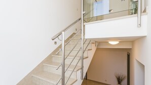 Un intérieur moderne avec un escalier, une balustrade en verre et un vase rempli de fleurs.
