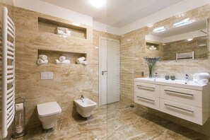Une salle de bain moderne équipée d’un bidet, de toilettes, d’un meuble-lavabo avec des tiroirs et d’un grand miroir.