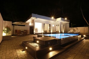 Un área de piscina moderna al aire libre con un jacuzzi, un comedor con sillas y una zona de estar cubierta.