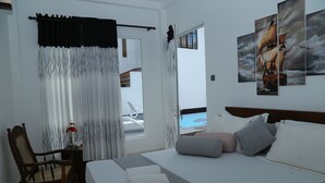 A hotel room with a bed, a chair, a small table with a vase, and a view of a pool and building through a window. - FIVE BEDROOM DELUXE VILLA WITH PRIVATE SWIMMING POOL (Habaraduwa)