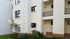 Ein mehrstöckiges Wohngebäude mit flacher Fassade, Balkonen und einem kleinen Gartenbereich mit pflegeleichten Pflanzen.