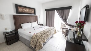 Ein Hotelzimmer mit einem großen Bett, einem Nachttisch, einem Schreibtisch mit Stuhl, einem Deckenventilator und einem Fenster mit Vorhängen.