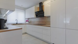 Ett modernt kök med vita skåp, en bänkskiva i trä, en svart köksfläkt och ett fönster med persienner.