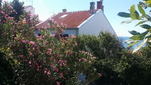 A building with a red-tiled roof and a white facade, surrounded by lush greenery and pink flowers. - "Apartment SEVEN" with Stunning Sea View (Dubrovnik)