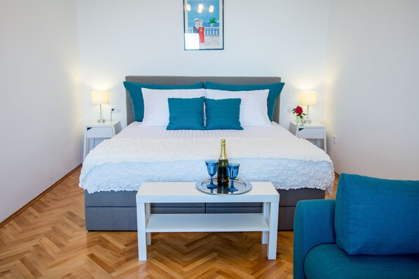 A neatly arranged bedroom with a bed, bedside tables, a bedside lamp, a small table with a bottle and glasses, and a chair. - "Apartment SEVEN" with Stunning Sea View (Dubrovnik)