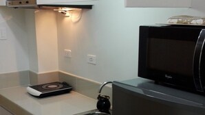 Una cocina compacta con armarios blancos, un refrigerador negro, un microondas y un horno integrado.