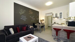 A modern living room with a sofa, a coffee table, and a dining area with a table and chairs. There is a kitchen area with a counter and stools. - Cozy two bedrooms apartment in vivid neighborhood  (Zagreb)