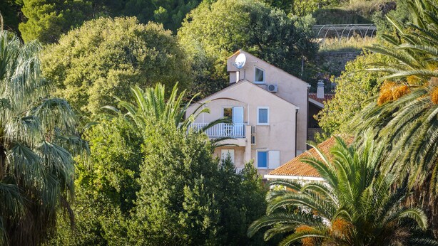 Un bâtiment à deux étages doté d’un balcon, entouré d’une végétation luxuriante et d’arbres.