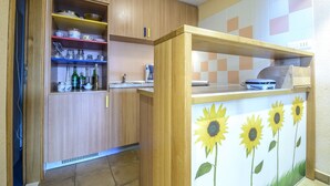 Une cuisine avec des meubles en bois, un plan de travail orné d’une fresque de tournesols et un pare-feu en carreaux.