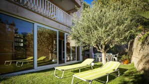 Une maison moderne avec une porte vitrée donnant sur un patio. On y trouve deux fauteuils de jardin jaunes posés sur la pelouse.