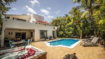 A modern house with a swimming pool, lounge chairs, and a hot tub.