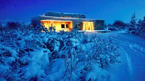 Een modern huis met een goed verlichte ingang, omringd door met sneeuw bedekte begroeiing.