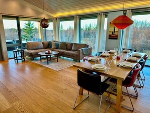 Ein moderner Essbereich mit einem Holztisch, gedeckt für sechs Personen, einer Couch und Blick ins Freie.