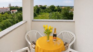 Ein Balkon mit einem gelben Tisch, zwei weißen Stühlen, einer Vase mit gelben Blumen und einer Champagnerflasche.