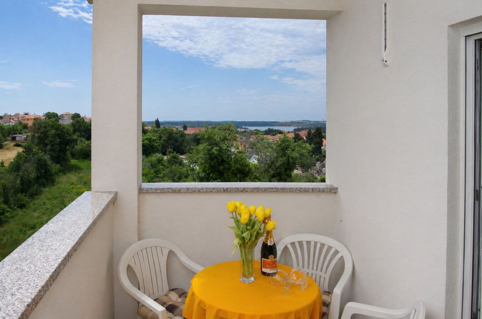 A balcony with a table, chairs, a vase of yellow flowers, and a bottle of champagne.