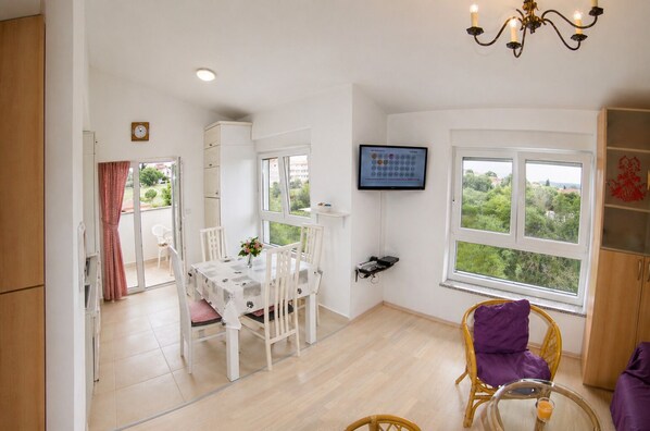A room with a dining table, chairs, a television, a window with a view, and a chandelier.